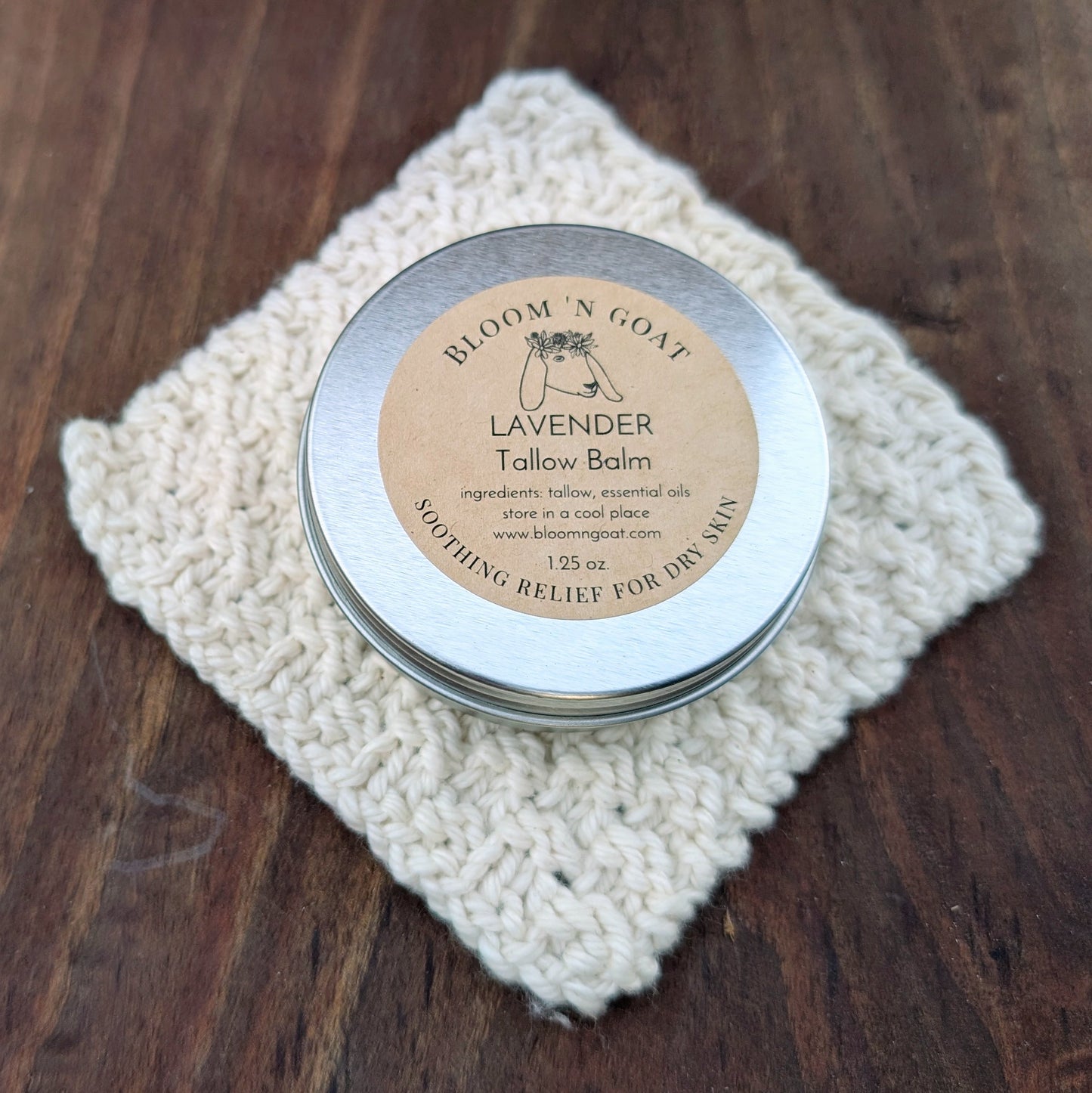 Bloom 'N Goat Lavender calming Tallow Balm tin on a handknit cloth with a dark walnut wooden background