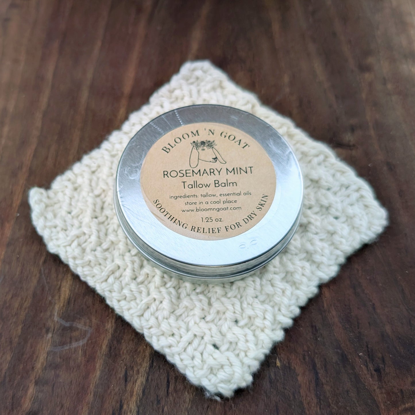 Bloom 'N Goat Rosemary Mint Tallow Balm tin perfect for tired feet on a handknit cloth with a dark walnut wooden background