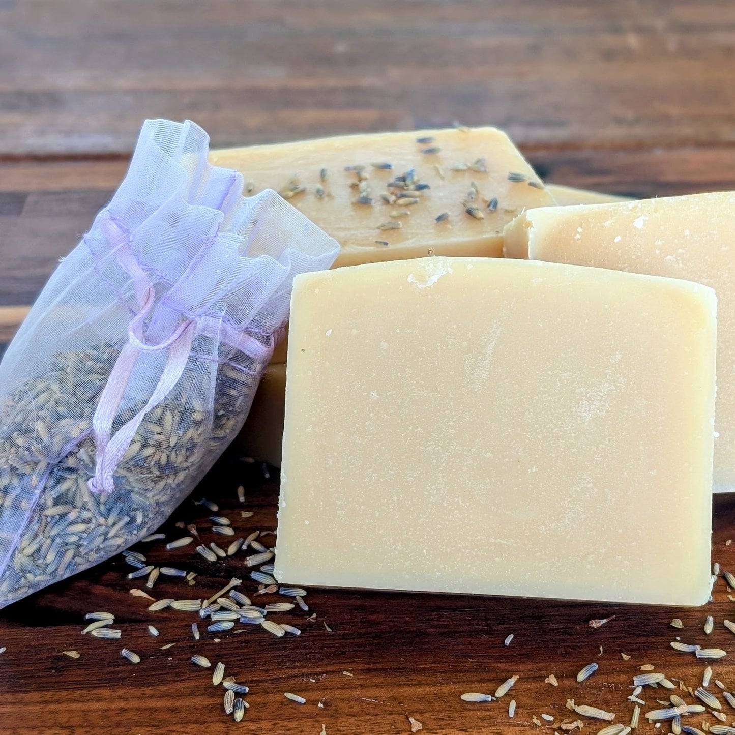 Bloom 'n Goat Lavender goat milk soap bars with lavender sachet and dried lavender on a rustic walnut wood surface