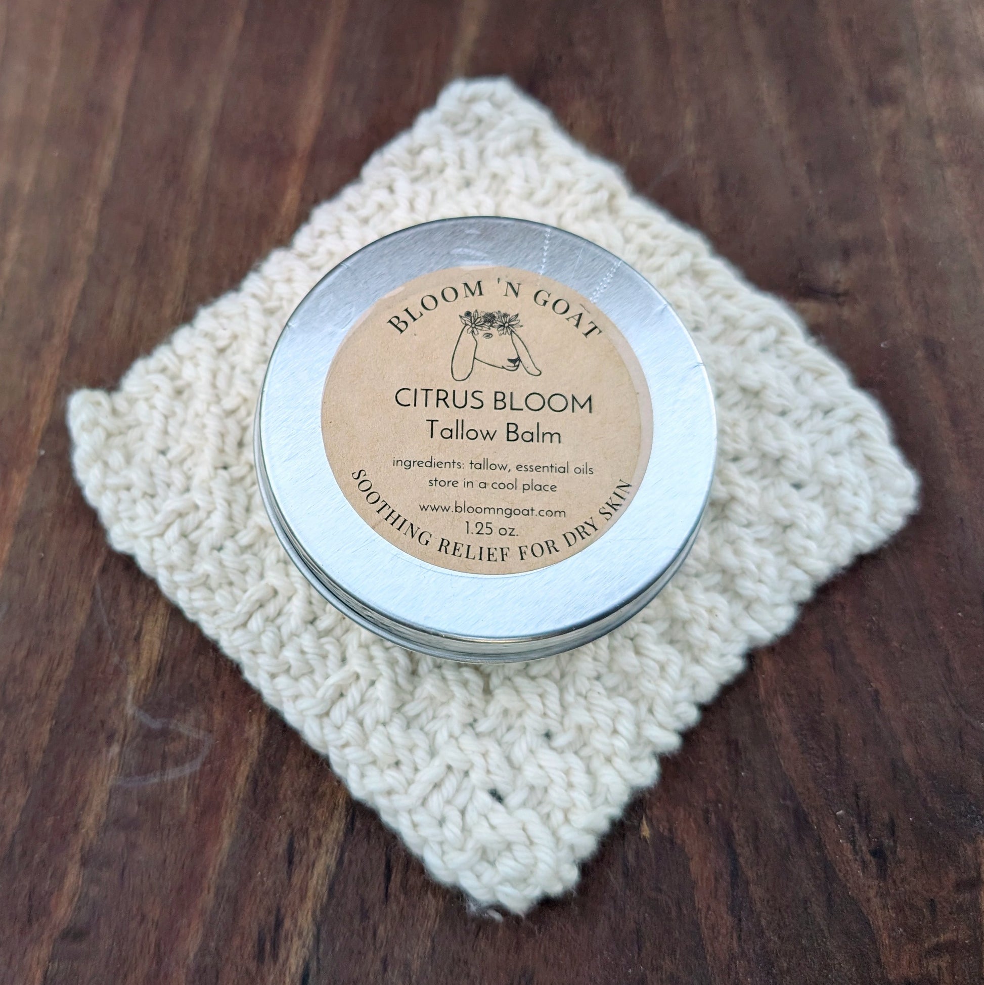 Bloom 'N Goat warm and grounding with frankincense Citrus Bloom Tallow Balm tin on a handknit cloth with a dark walnut wooden background