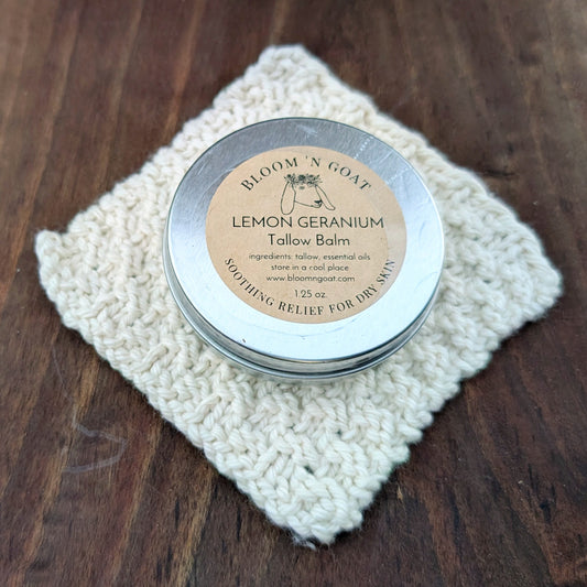 Bloom 'N Goat Lemon Geranium vintage floral Tallow Balm tin on a handknit cloth with a dark walnut wooden background