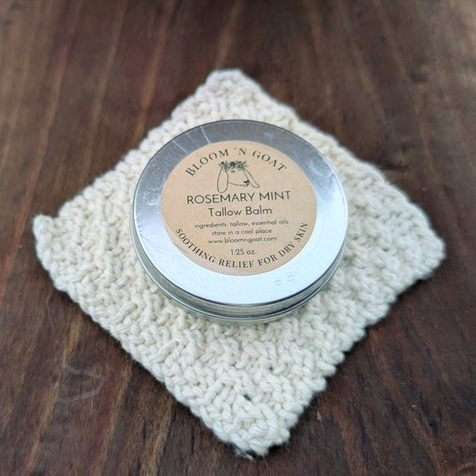 Bloom 'N Goat Rosemary Mint Tallow Balm tin perfect for tired feet on a handknit cloth with a dark walnut wooden background