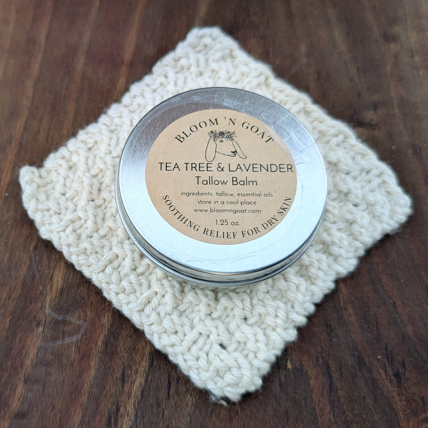 Bloom 'N Goat Tea Tree and Lavender Tallow Balm tin for sensitive skin on a handknit cloth with a dark walnut wooden background