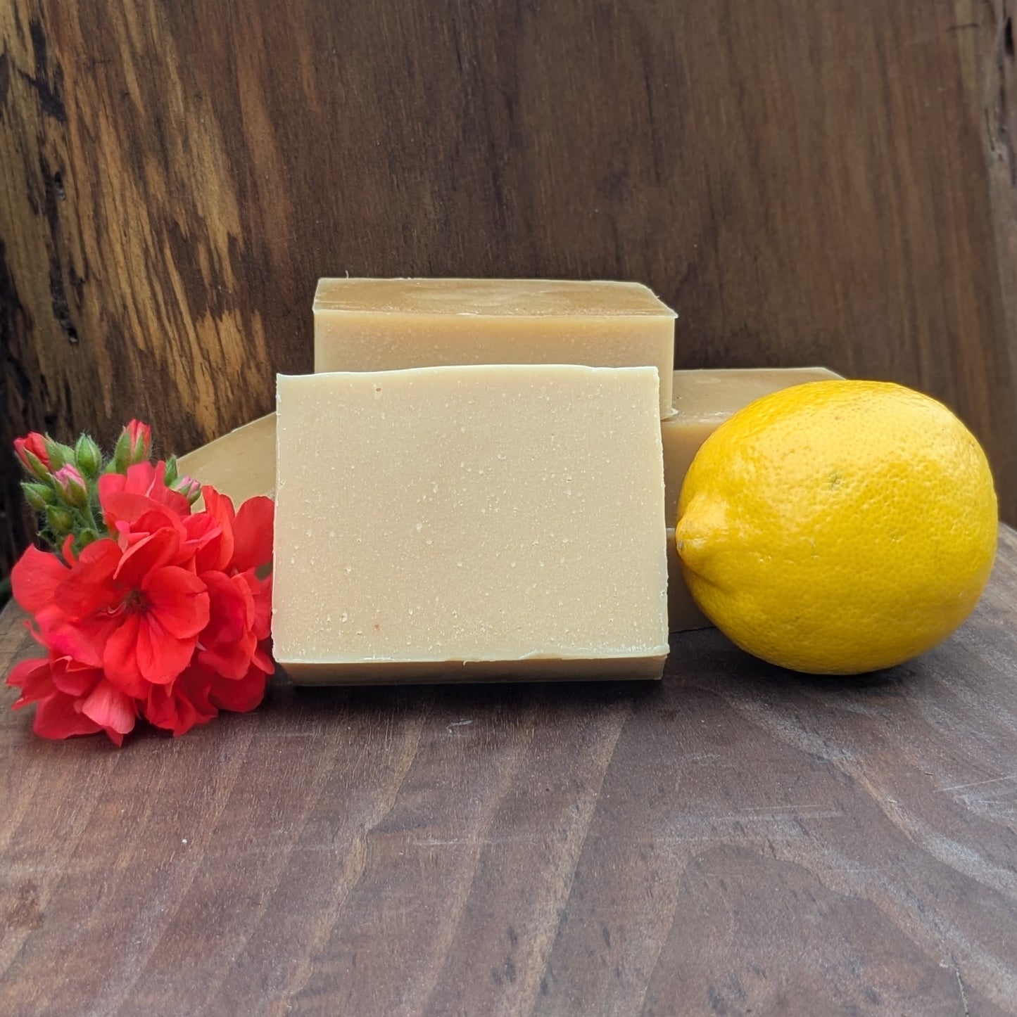 Bloom 'n Goat Lemon Geranium goat milk soap bars with fresh lemon and geranium bloom on a walnut wood background